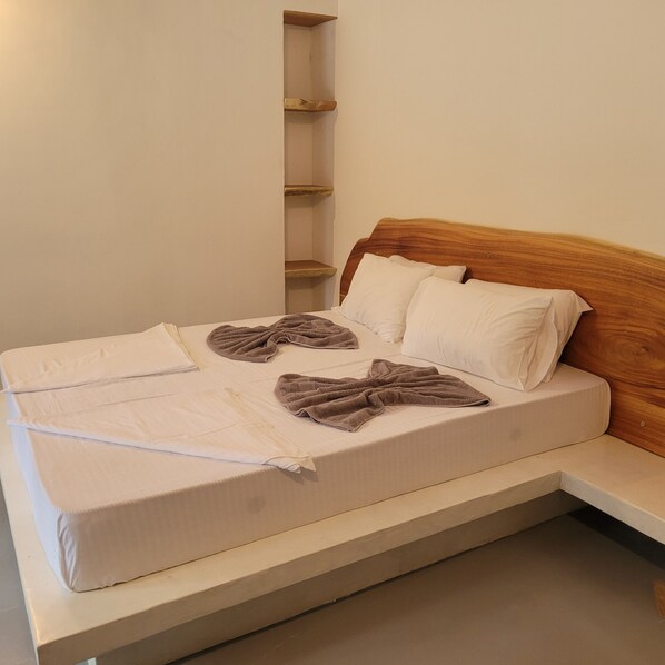 A single bed with a wooden headboard, white bedding, and two brown towels.