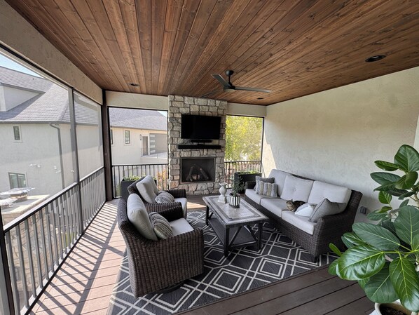 A covered outdoor seating area with a stone fireplace, wicker furniture, and a television mounted on the wall. - MIZ-ZOU football weekend home
Awesome  house on Hole #7 at Old Hawthorne (Columbia)
