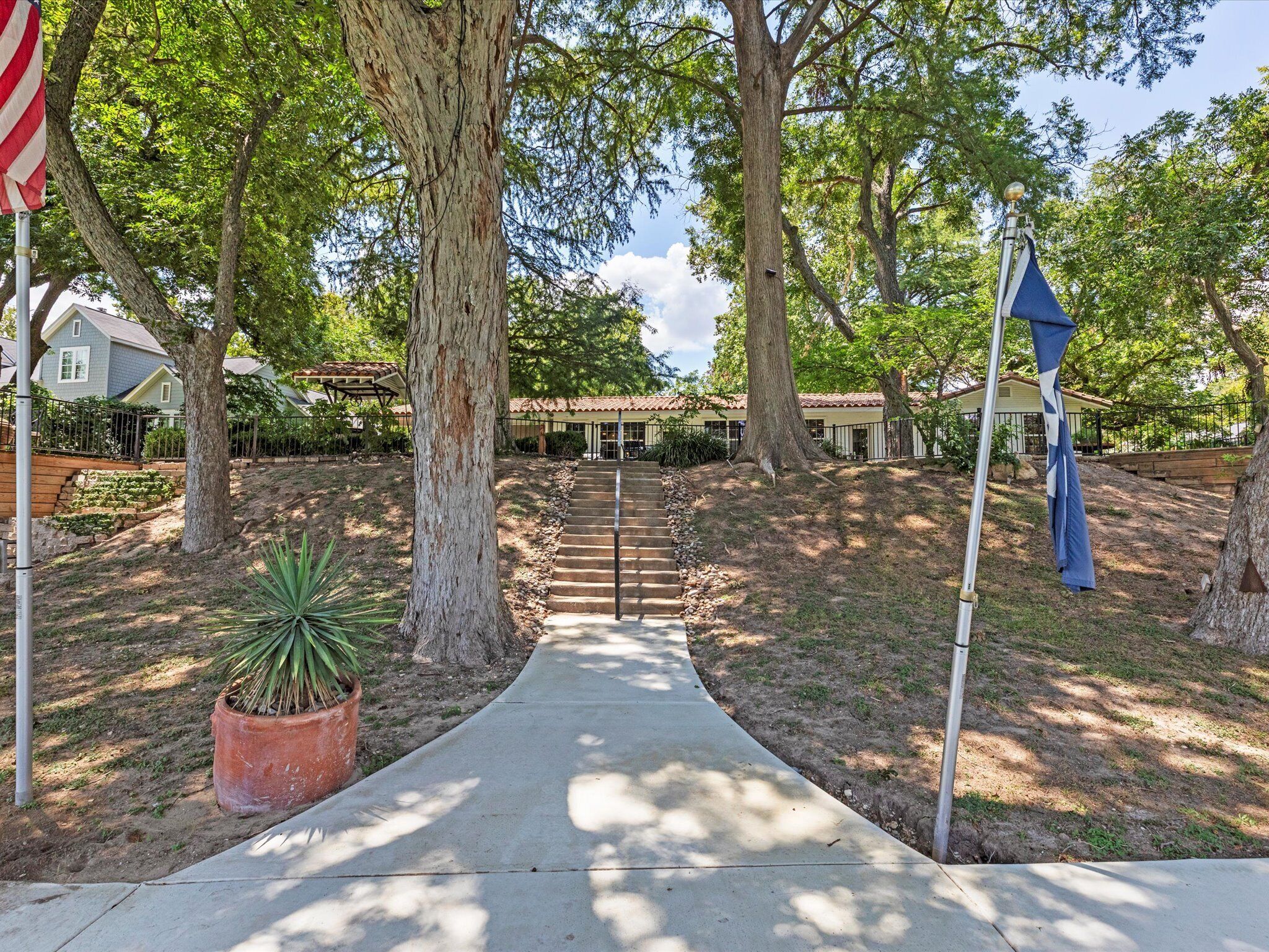 A pathway leading to a building with a covered patio area, surrounded by trees and a flagpole.