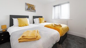 A hotel room with two beds, a radiator, a window with blinds, and a painting on the wall. - 6 Tannery House | Wi-Fi | Parking | Contractors (Freckleton)
