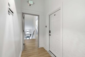 Ein Flur mit einer weißen Tür, einem Fluchtwegschild und einer Treppe im Hintergrund.