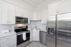 Eine moderne Küche mit weißen Schränken, einem Edelstahl-Kühlschrank, einer Mikrowelle, einem Backofen und einem Geschirrspüler.