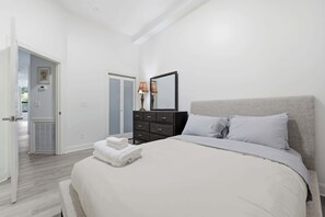 Ein Schlafzimmer mit einem Bett, einem Schminktisch, einem Spiegel und einer Tür zu einem weiteren Raum.
