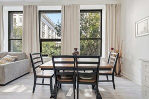 A dining area with a table and chairs, large windows, and a view of buildings and trees. - Front Row Loft | Vaulted Ceilings | Free Parking (Louisville)
