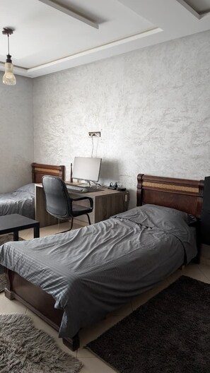 Une chambre avec deux lits, un bureau avec un ordinateur et une chaise.