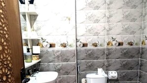 Baño con lavamanos, inodoro y zona de ducha de mármol, con detalles en azulejos de mármol y una puerta de madera.