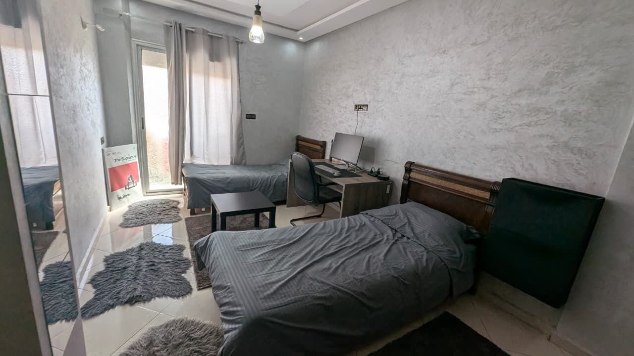 A bedroom with two beds, a desk, a chair, and a computer.