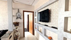 Una sala moderna con una televisión de pantalla plana montada en una pared con textura, un jarrón decorativo con flores y un reloj con diseño de la Torre Eiffel.