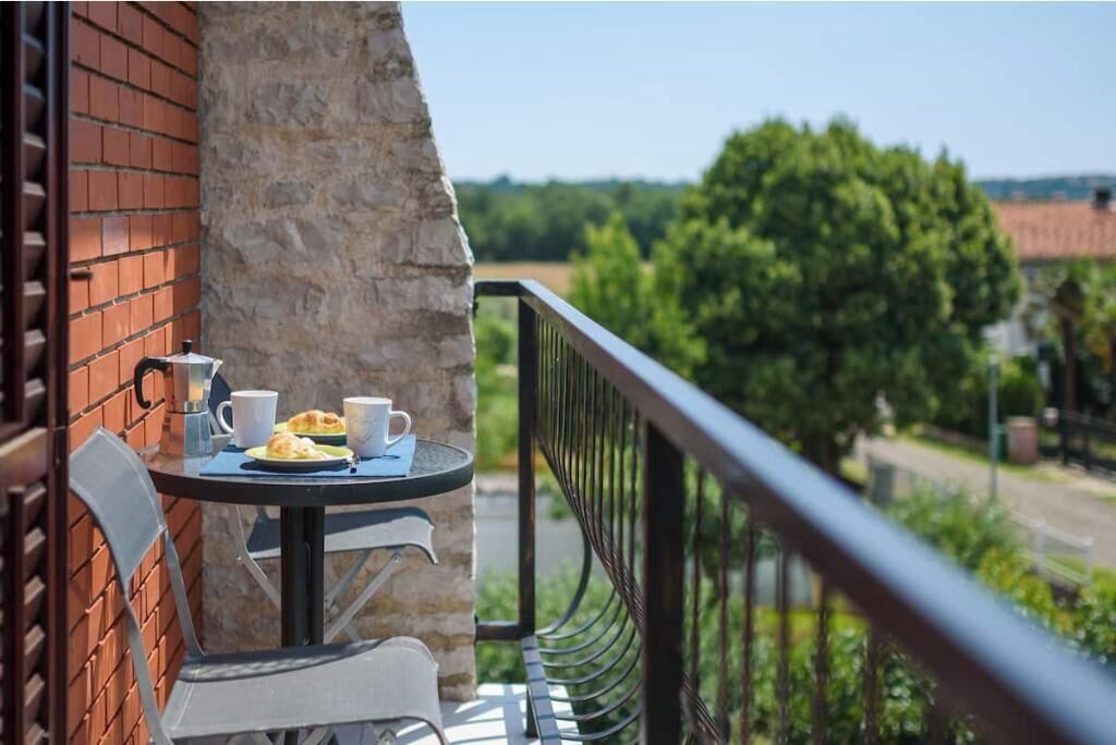 A balcony with a table set for two, a brick wall, and a view of greenery and buildings in the distance.