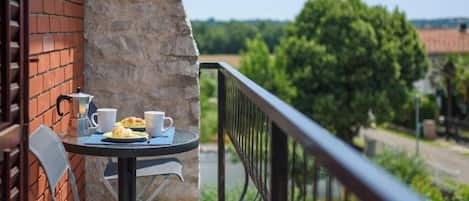 A balcony with a table set for two, a brick wall, and a view of greenery and buildings in the distance.