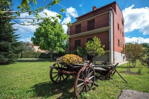 Ein zweistöckiges Gebäude mit roter Backsteinfassade und einem Balkon. Vor dem Gebäude steht ein hölzerner Wagen mit einer Blumenkomposition.