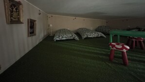 Een kamer met een groen tapijt, een bed met gekleurde kussens, een tafeltje en een rode paddenstoel.