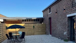Een terras met een tafel en stoelen, een houten omheining en een bakstenen gebouw.
