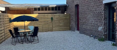 A patio area with a table and chairs, a wooden fence, and a brick building.