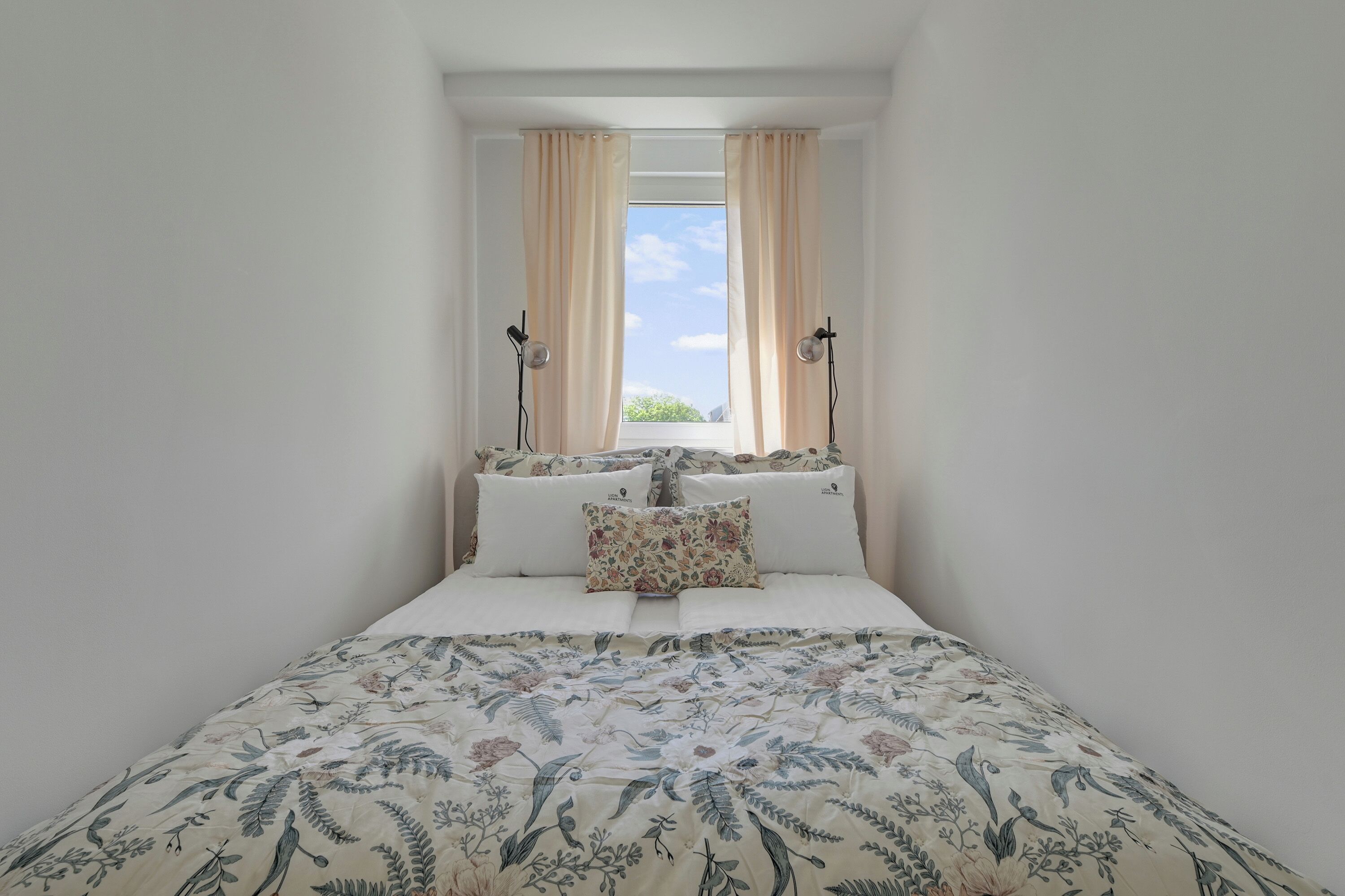 Una habitación pequeña con una cama, dos lámparas y una ventana con cortinas.