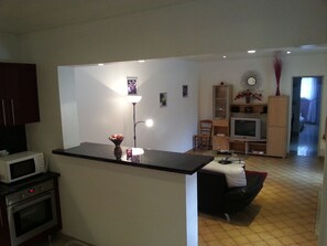 A modern kitchen with a microwave, oven, and a small island with a vase. There is a living area with a sofa, TV, and a bookshelf. - 3-bedroom vacation rental, 10 minutes from Jonzac, fully fenced (Rouffignac)