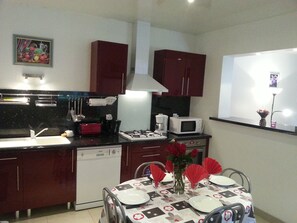 A compact kitchen with a dishwasher, microwave, and stove, a dining table set with red napkins, and a vase with flowers. - 3-bedroom vacation rental, 10 minutes from Jonzac, fully fenced (Rouffignac)
