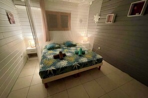 A bedroom with a bed, a nightstand, a window with curtains, and a wall-mounted shelf. - Villa Morphy, ocean view, pool, beach 3 minutes away, between DESHAIES and BOUILLANTE (Pointe-Noire)