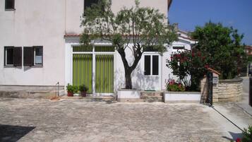 A building with a stone-paved courtyard, a tree, and potted plants.