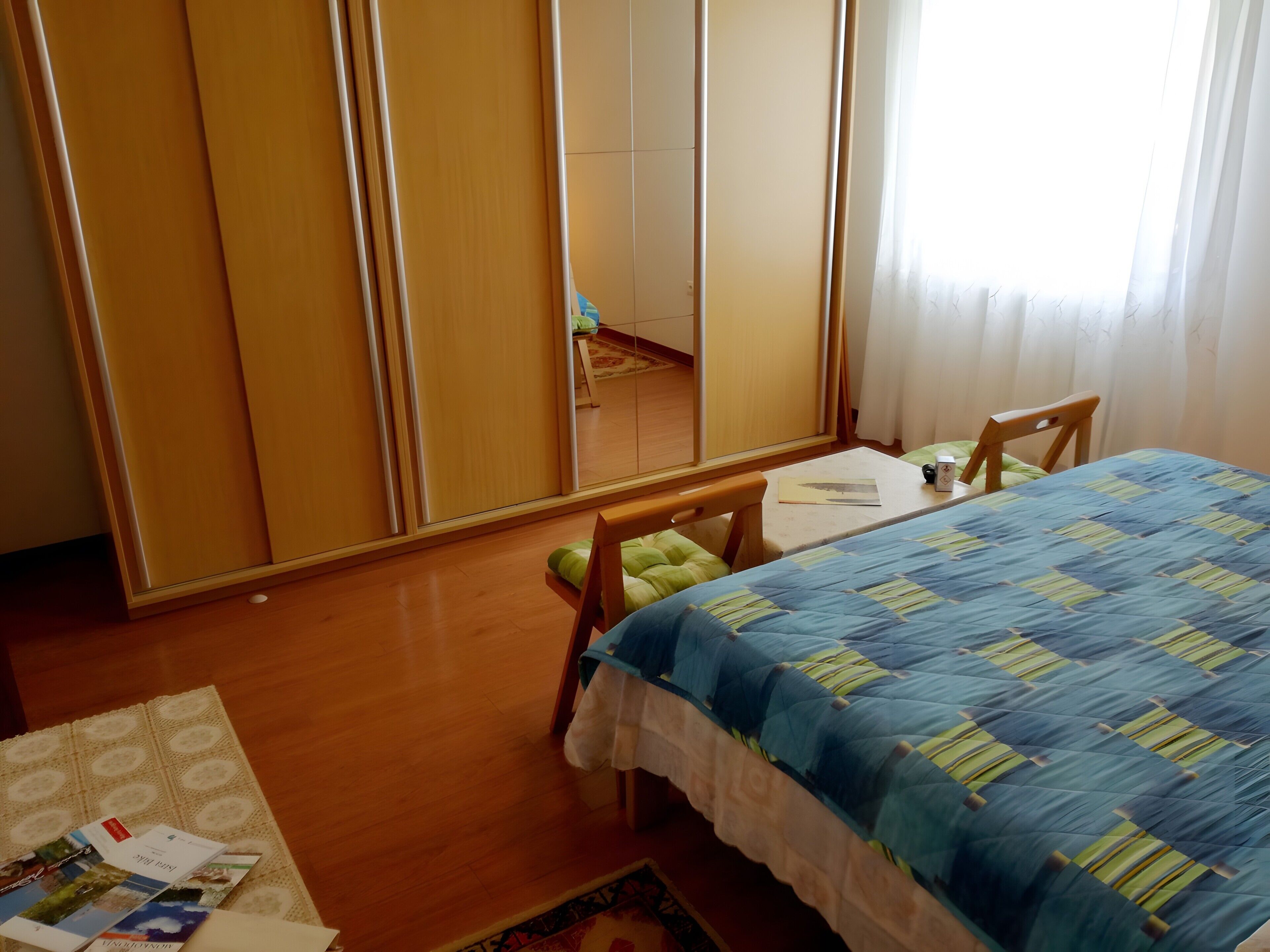 A bedroom with a bed, a wooden wardrobe, a small table, and a chair.