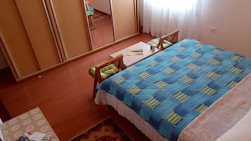 A bedroom with a bed, a chair, a small table, a mirror, and a window with curtains.