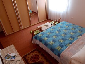 Ein Schlafzimmer mit Bett, Sessel, Nachttisch, Spiegel und einem Fenster mit Vorhängen.