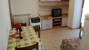 A small room with a dining table set for two, a television on a shelf, and a radiator under the window. - Apartment '3 Pax  Near Pebble Beach' with Balcony, Wi-Fi and Air Conditioning (Rovinj)