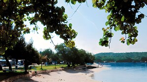 A beach with a stone wall, trees, and a clear view of the water. - Apartment '3 Pax  Near Pebble Beach' with Balcony, Wi-Fi and Air Conditioning (Rovinj)