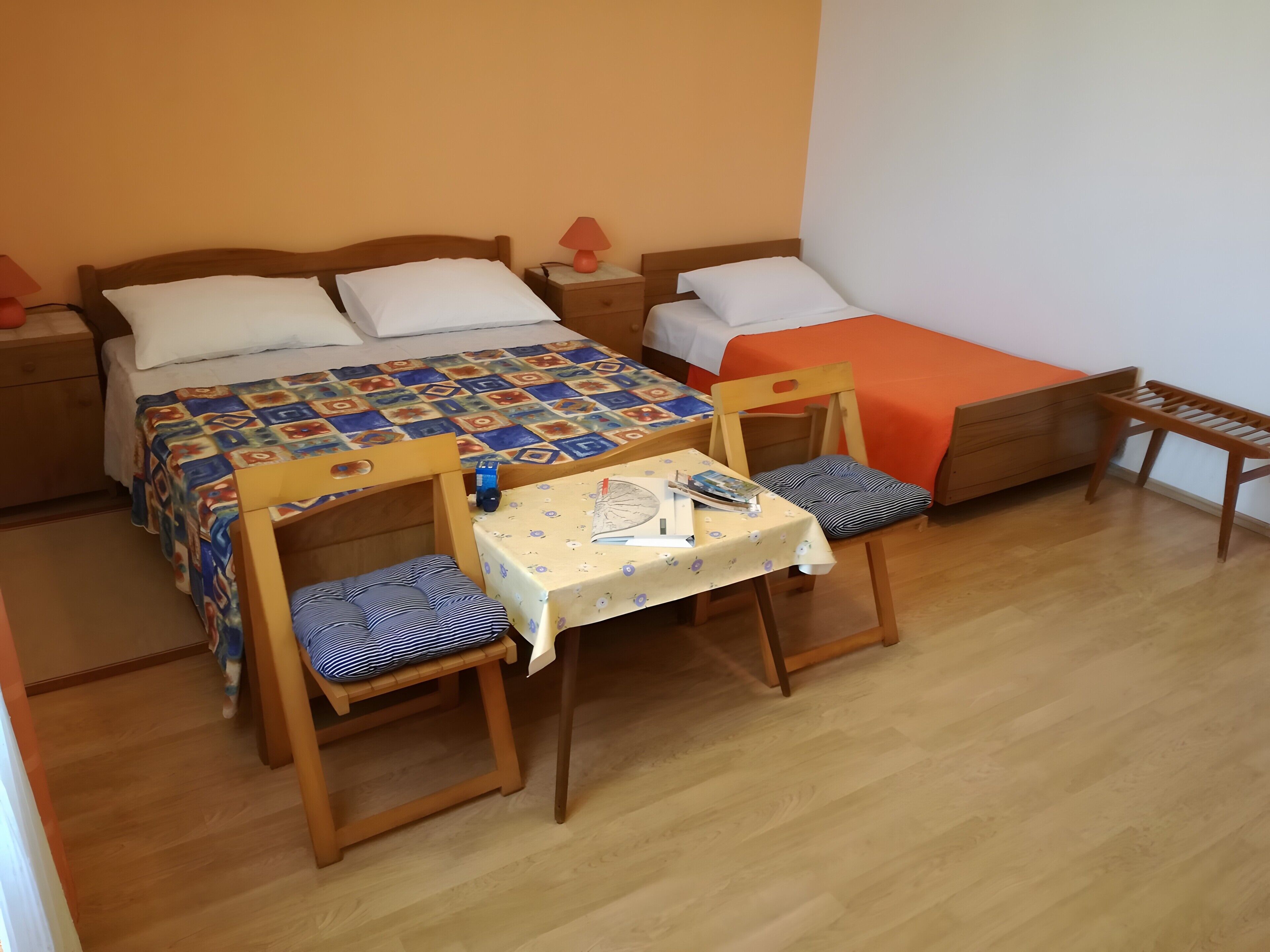A room with two beds, a table with chairs, and a small wooden stool.