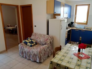 Ein kompakter Wohnbereich mit Sofa, Esstisch, Küchenzeile und einer Tür zu einem weiteren Zimmer.