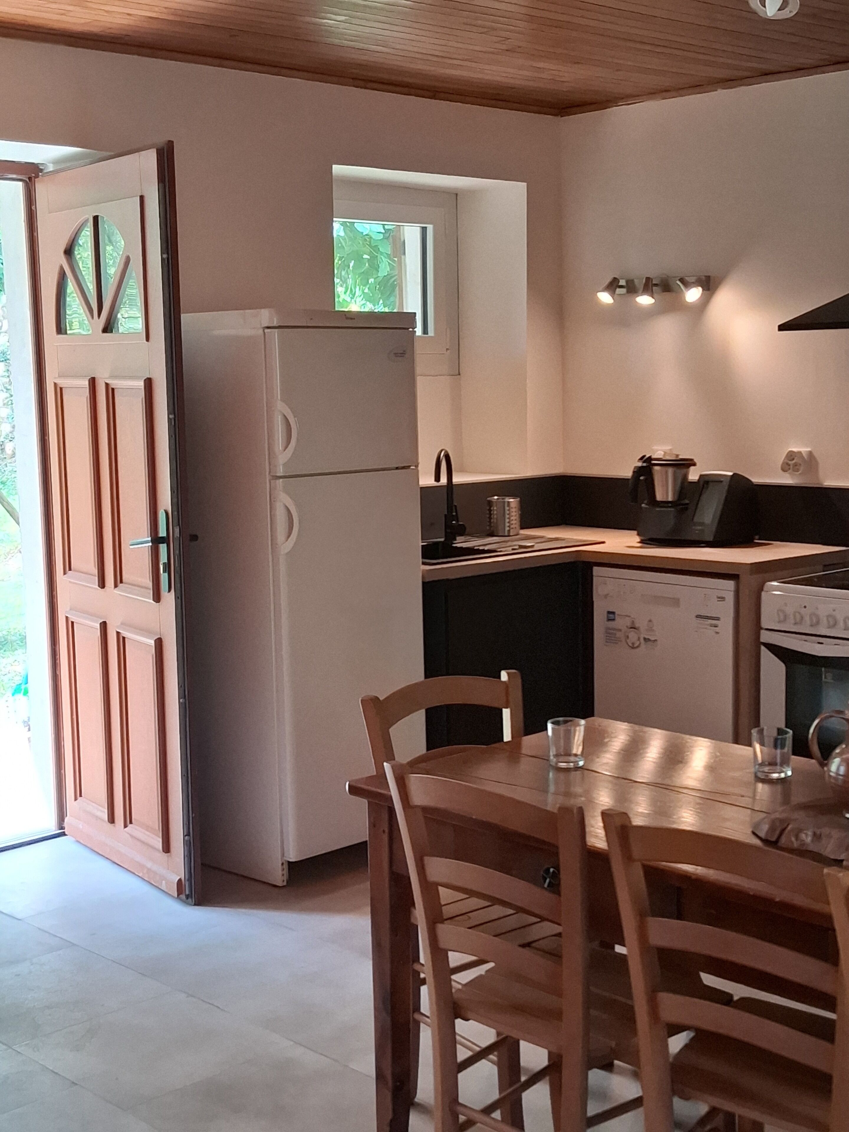 Una cocina compacta con refrigerador, estufa y lavamanos. Hay una mesa de comedor con sillas.