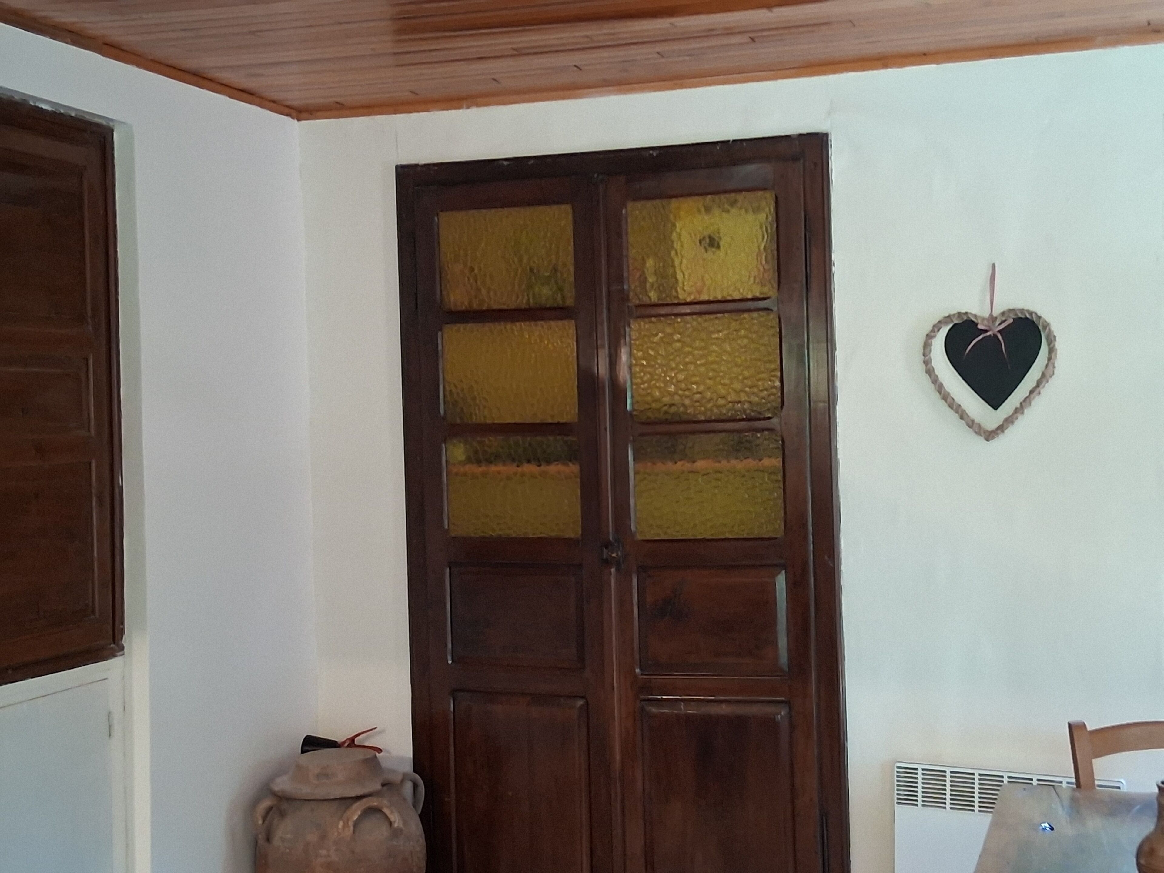 Una puerta de madera con paneles de vidrio, un adorno con forma de corazón colgado en la pared y una maceta pequeña en el suelo.
