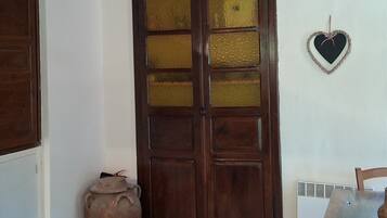 Una puerta de madera con paneles de vidrio, un adorno con forma de corazón colgado en la pared y una maceta pequeña en el suelo.