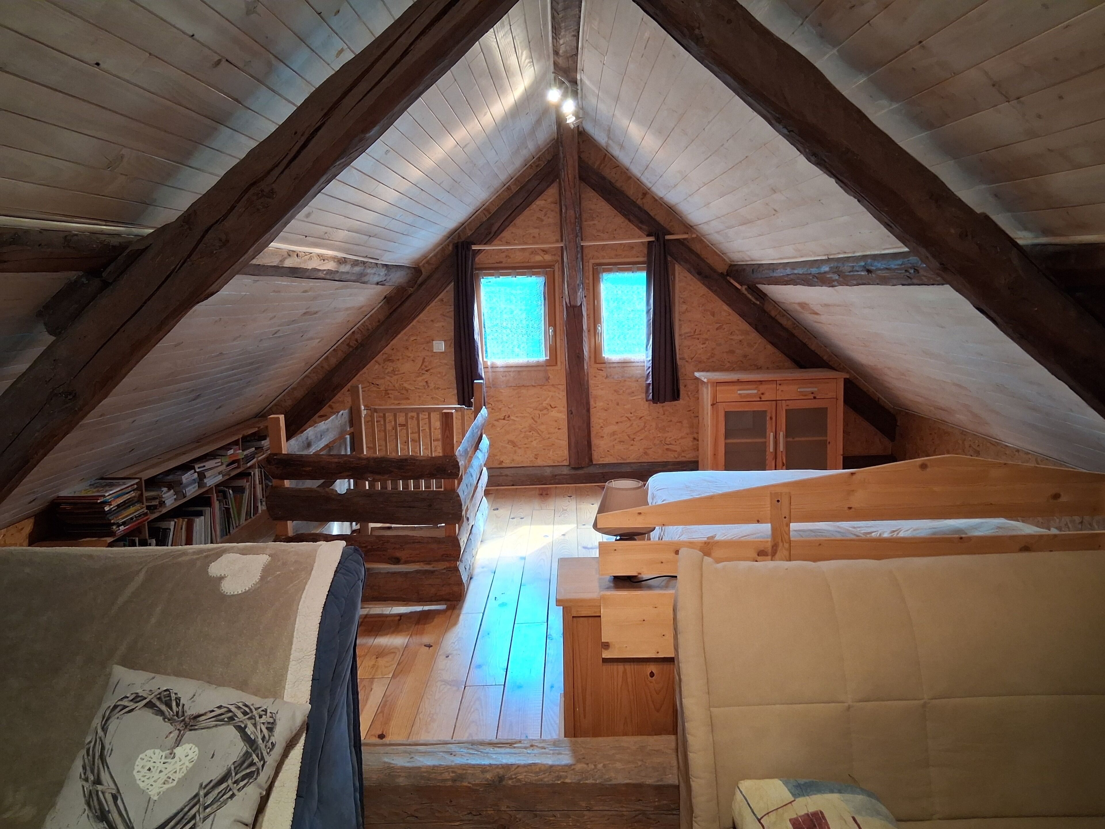 Un dormitorio en el ático con techo inclinado, vigas de madera, una cama literera, un escritorio y una ventana.
