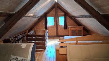 Un dormitorio en el ático con techo inclinado, vigas de madera, una cama literera, un escritorio y una ventana.