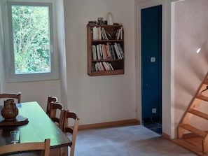 Ein Essbereich mit Tisch, Stühlen, einem Bücherregal und einem Fenster mit Blick auf Bäume.