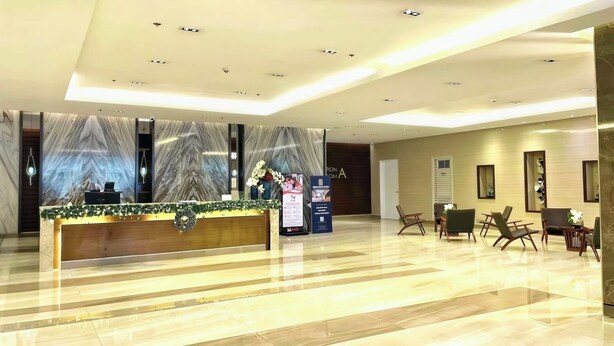 Ein Hotel-Empfangsbereich mit einem Marmor-Empfangstresen, einem digitalen Bildschirm und einer Sitzecke mit Sesseln.