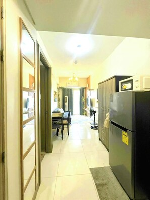 A kitchen with a refrigerator, a dining area with a table and chairs, and a hallway leading to a living room. - Fully furnished cozy 1-bedroom condo unit with AC for a staycation in Pasay City (Pasay City)