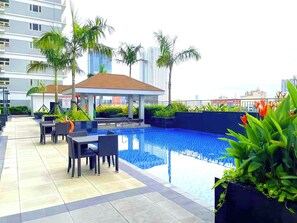 Un área de piscina en la azotea con sillones, asientos y vistas al horizonte de la ciudad.