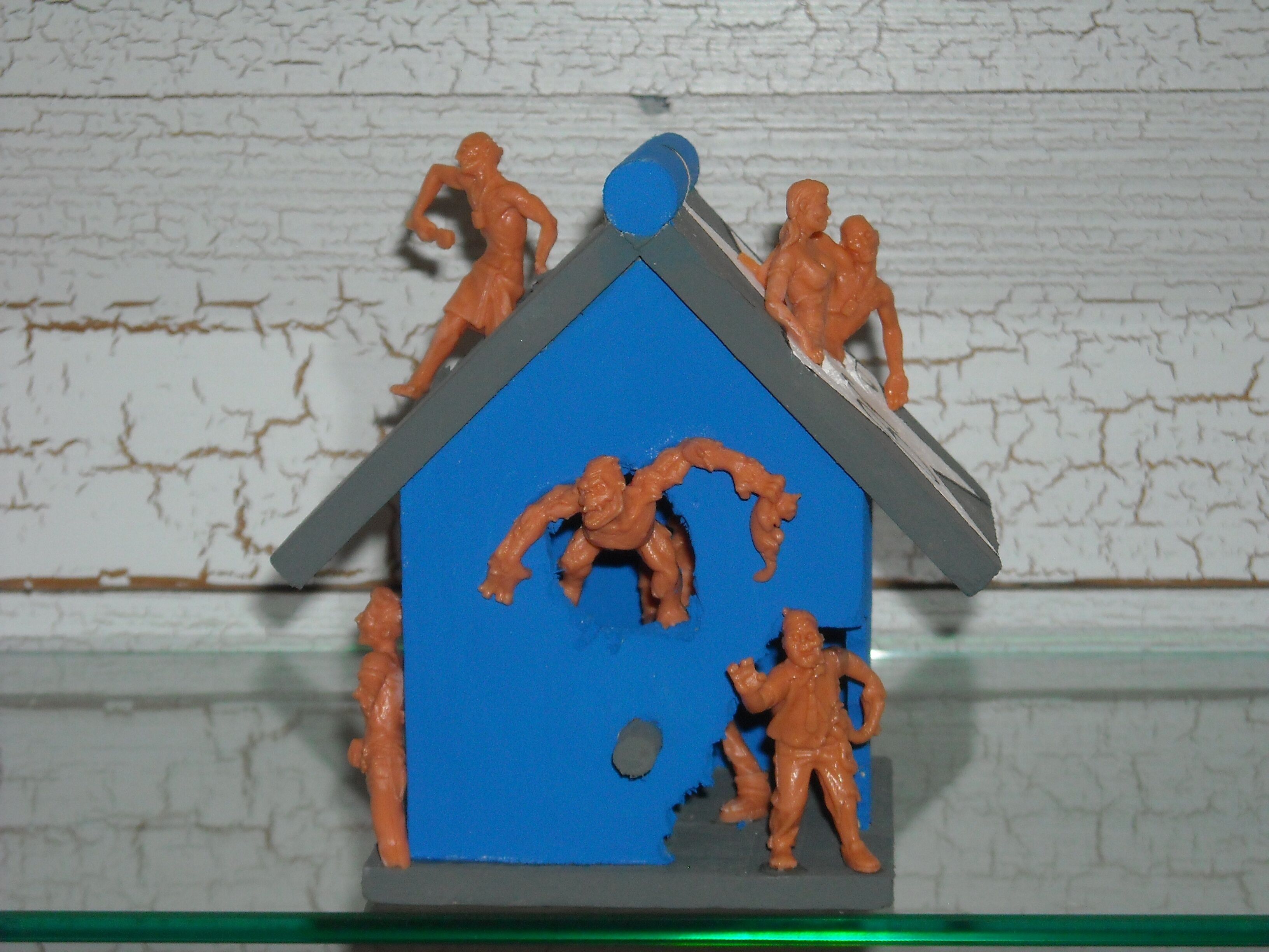 A toy house with figures on top and a figure standing in front.