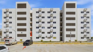 Un edifici residencial de diversos pisos amb balcons, un pàrquing i un cel serè.