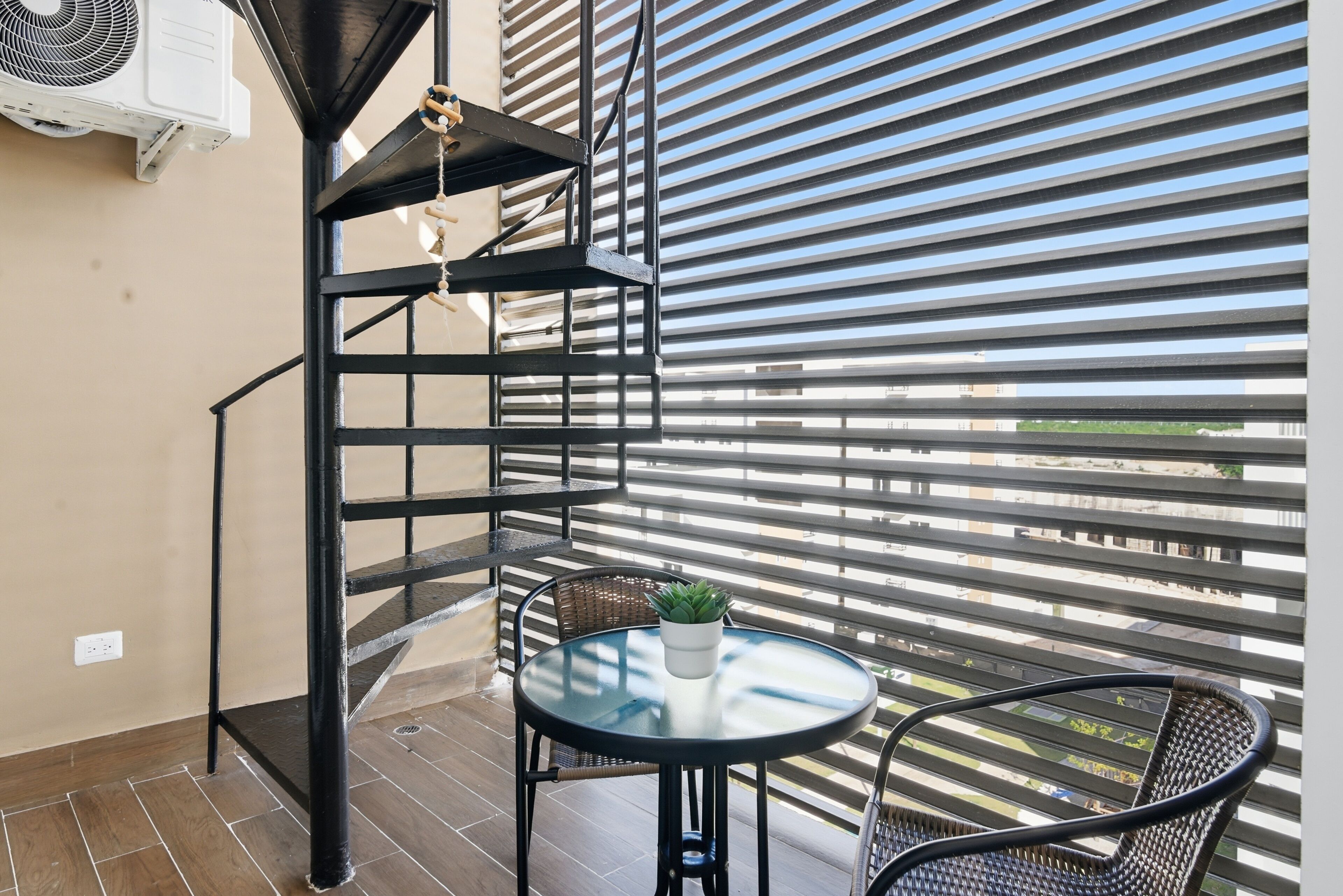A balcony with a metal spiral staircase, a small round table with a potted plant, and a wicker chair.