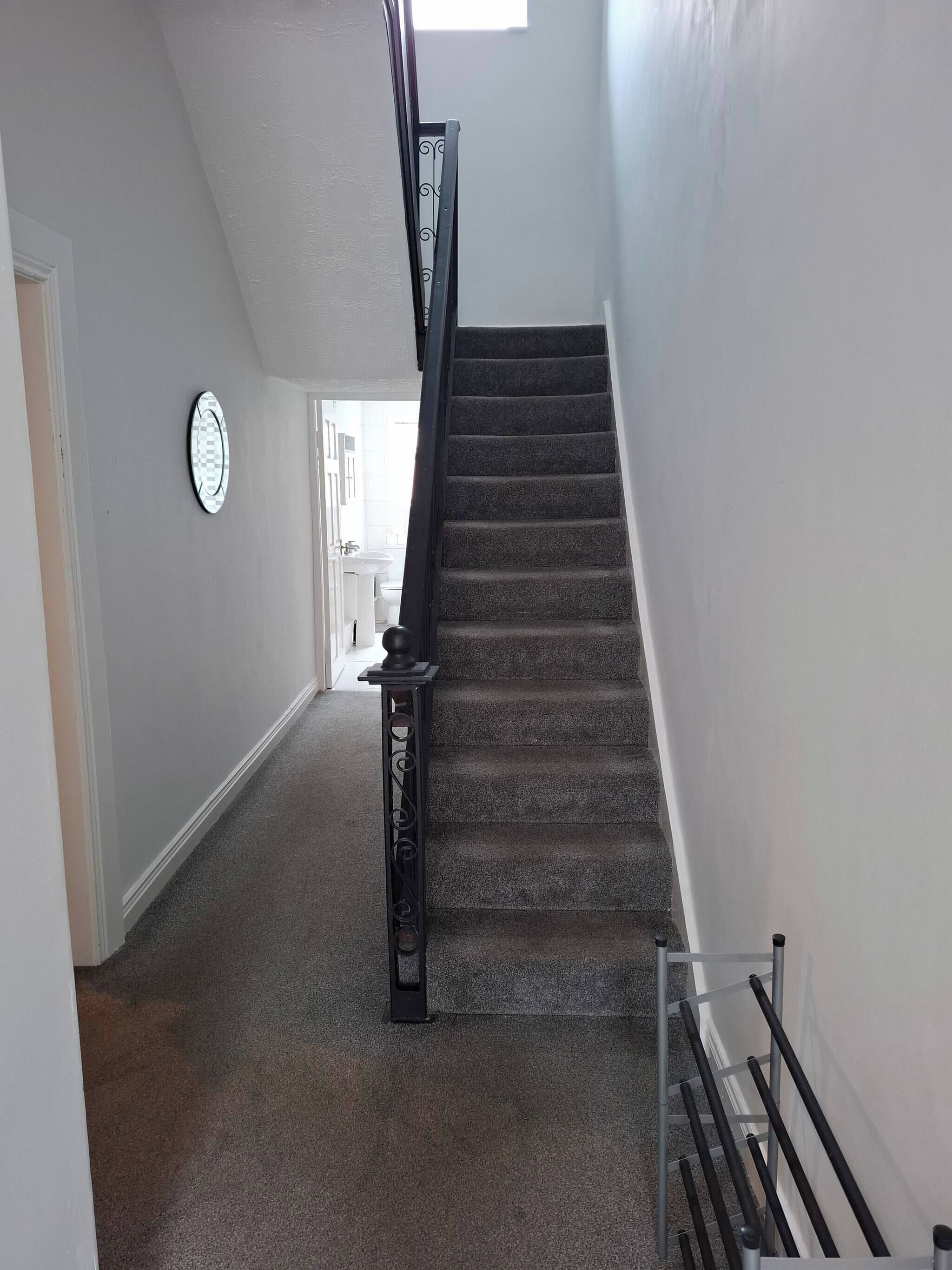Una escalera alfombrada con barandilla que conduce a una habitación con una puerta blanca y un ventanal.