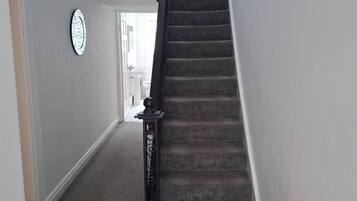 Una escalera alfombrada con barandilla que conduce a una habitación con una puerta blanca y un ventanal.