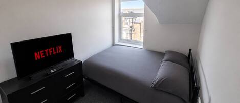 A bedroom with a bed, a TV, and a window.