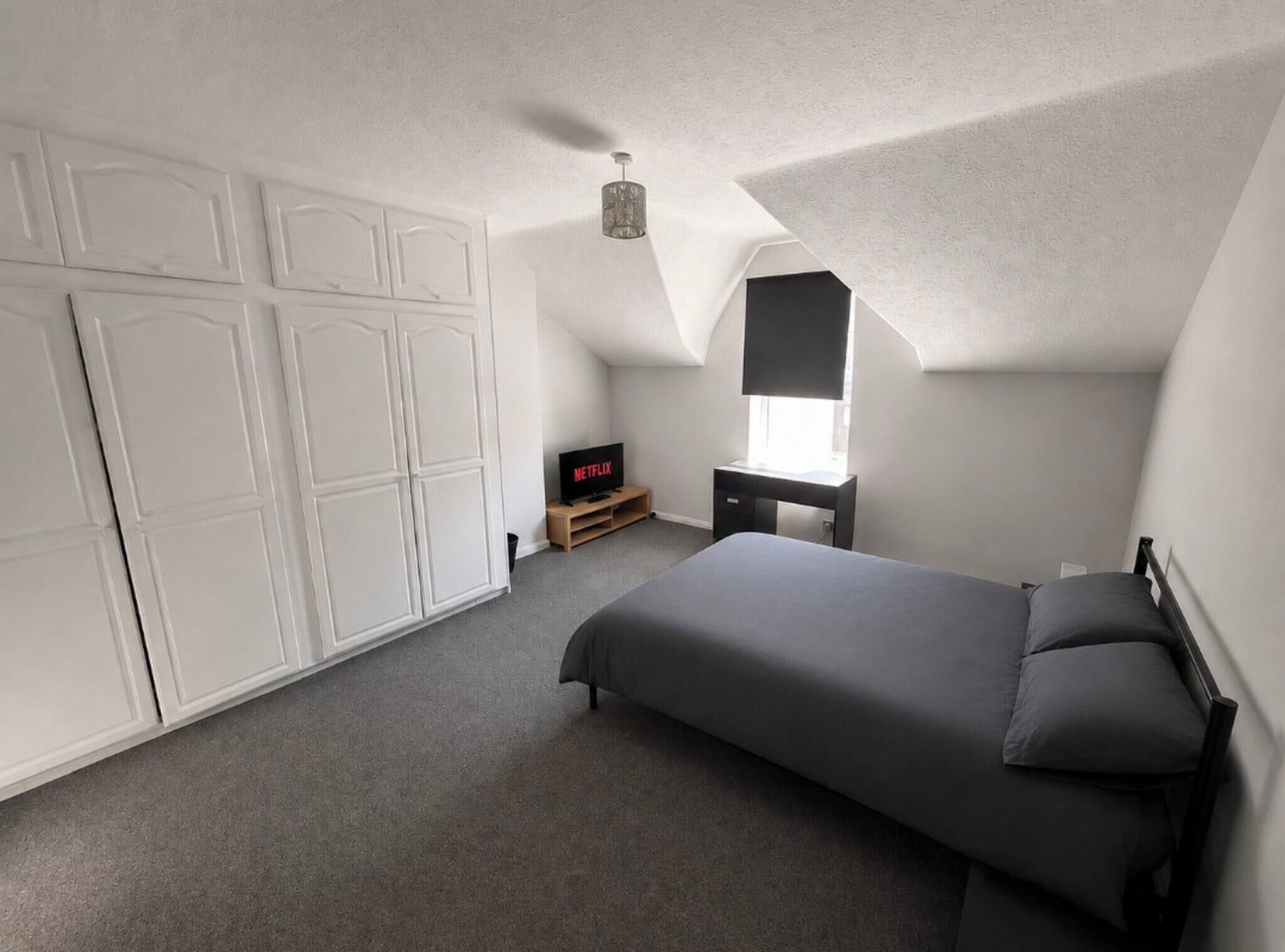 Une chambre à coucher avec un lit, une armoire, une télévision et un bureau.