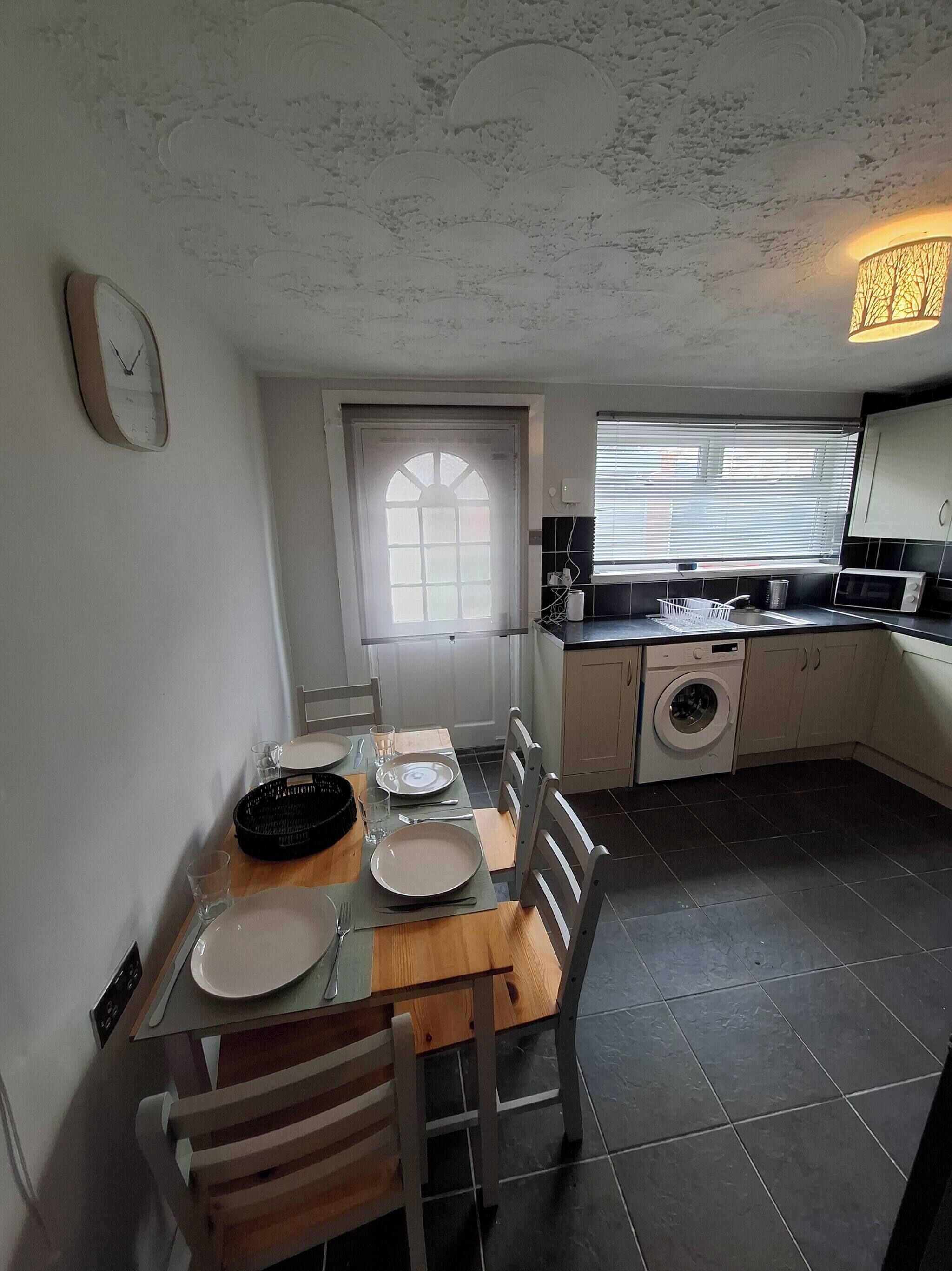 A compact kitchen with a dining area, a washing machine, and a window with blinds.