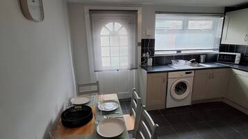 A compact kitchen with a dining area, a washing machine, and a window with blinds.