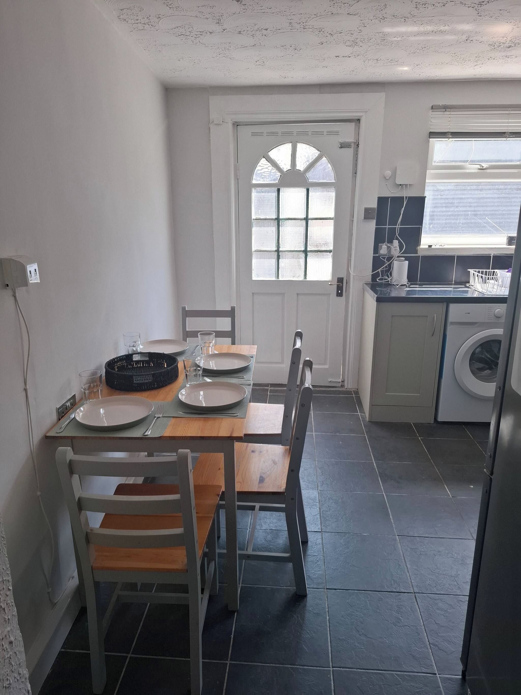 A compact kitchen with a dining area, a washing machine, and a window with blinds.