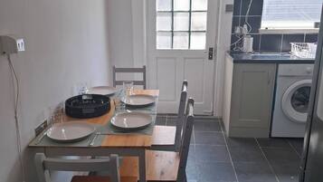A compact kitchen with a dining area, a washing machine, and a window with blinds.